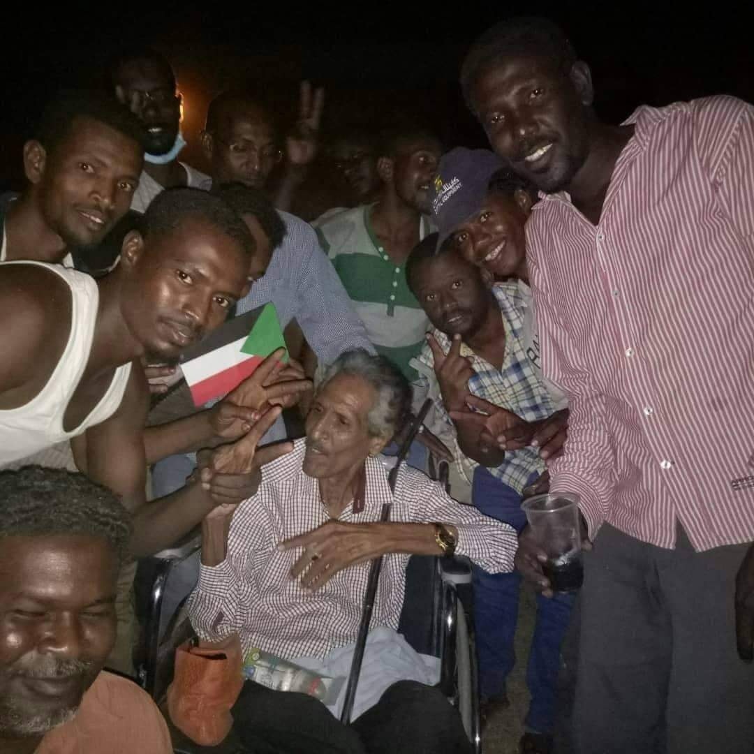 الممثل السوداني الكبير نبيل متوكل على كرسي متحرك وسط مجموعة من الشباب