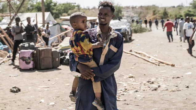 رجل يحمل طفلًا ونازحون سودانيون.jpg