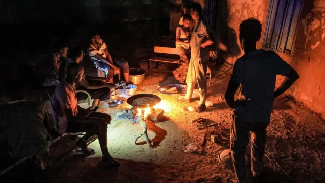 TOPSHOT - People sit around food cooking on a bonfire at a school that has been transformed into a shelter for people displaced by conflict in Sudan's northern border town of Wadi Halfa near Egypt late on September 11, 202.jpg