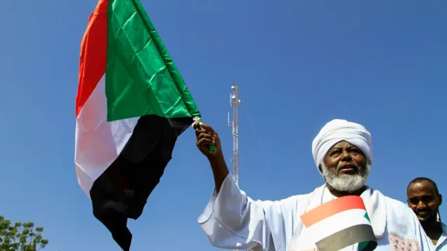 سوداني في الزي التقليدي يحمل علم السودان.jpg